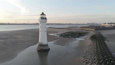 aerial right orbit view across british lighthouse breakers and coastal shipyard cranes sunrise skyline