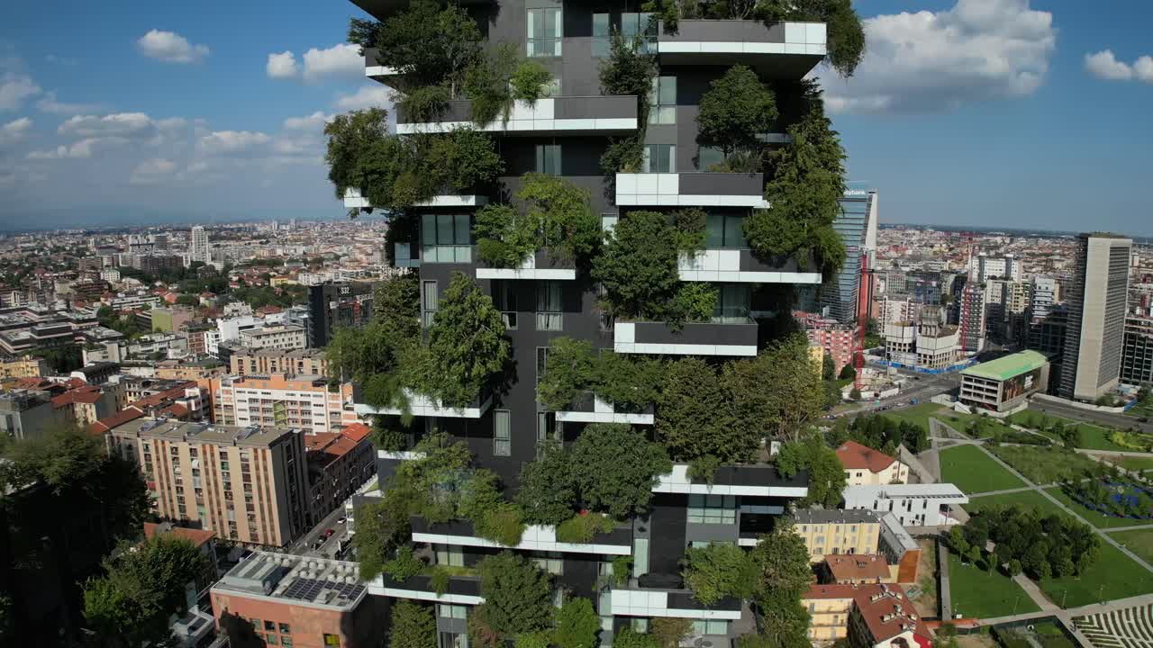 Drone captures a city-center building adorned with vertical forest greenery, surrounded by high-rise and low-rise structures, blending nature with urban architecture in striking detail.
