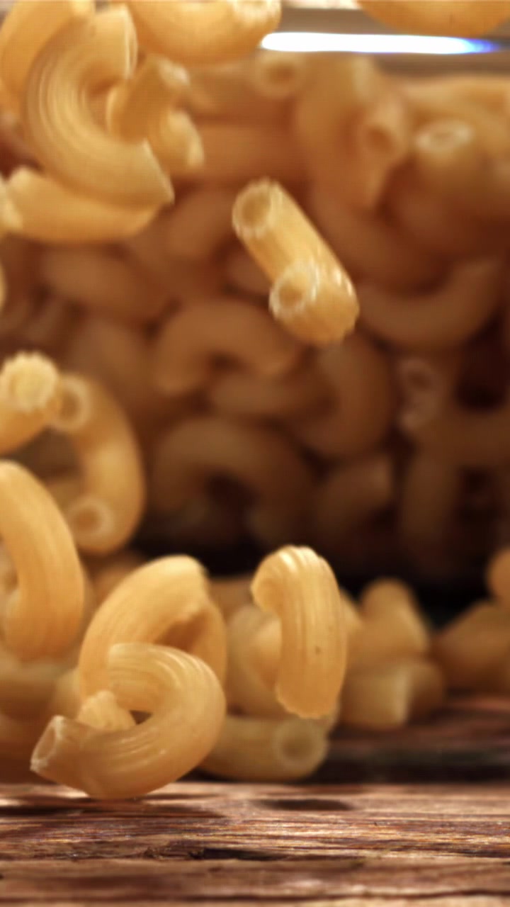 Maccheroni secchi che cadono al rallentatore su una superficie di legno