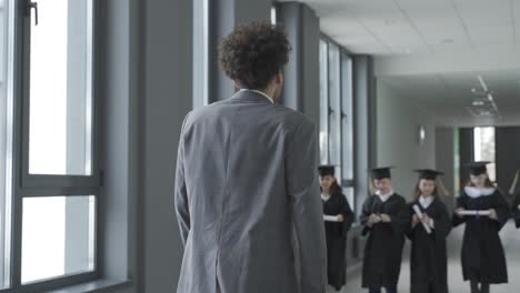 모타르보드와 가운을 입은 행복한 다인종 미취학 학생들이 선생님에게 인사합니다.