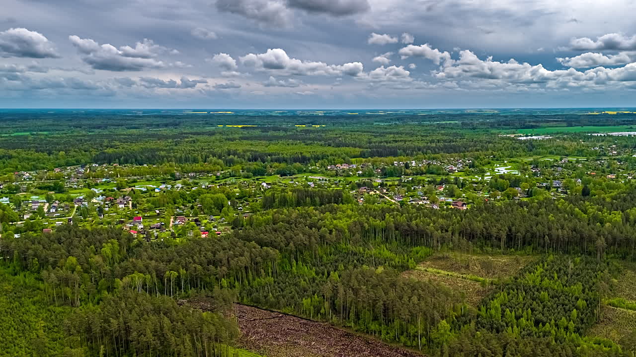 Green vibrant forest and flowing cloudscape over country village, aerial time lapse view