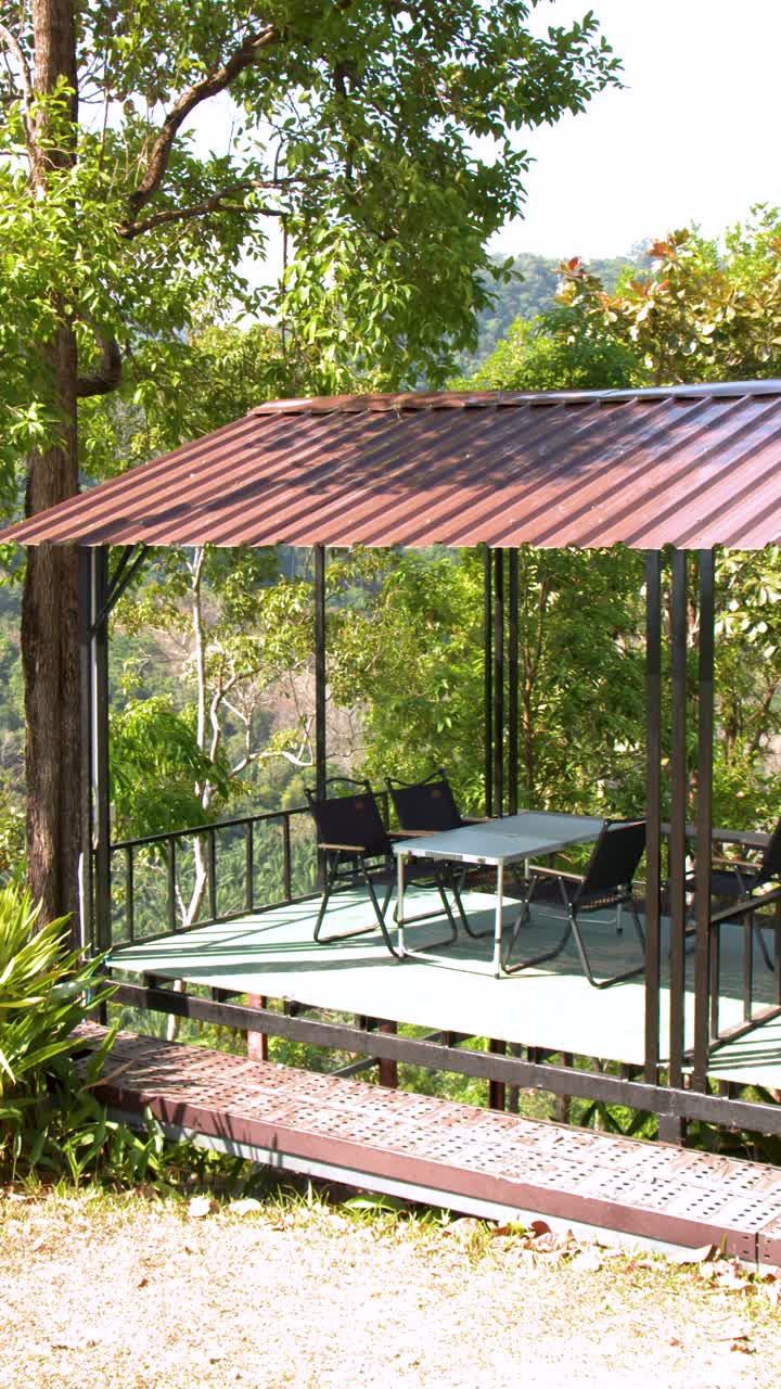 A slow zoom out reveals a metal roof pavilion overlooking a lush tropical jungle landscape