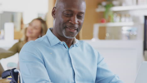 Mature-Businessman-In-Wheelchair-Sitting-At-Desk-Working-On-Laptop-In-Busy-Office