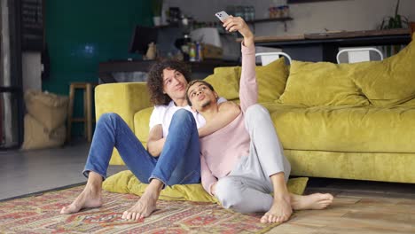 pareja gay romántica sentada en el suelo juntos, tomando una selfie con un teléfono inteligente