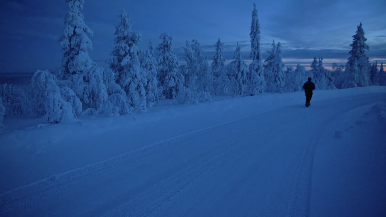 A Young Man Wearing A Black Winter Suit And Backpack Walking On A Frosted Ground Full Of Snow In Finland - Wide Shot