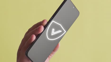 person holding a mobile phone where the animation of security shield appears, yellow background