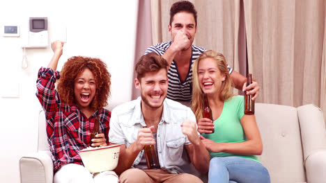 smiling friends watching tv while eating popcorn and drinking beer