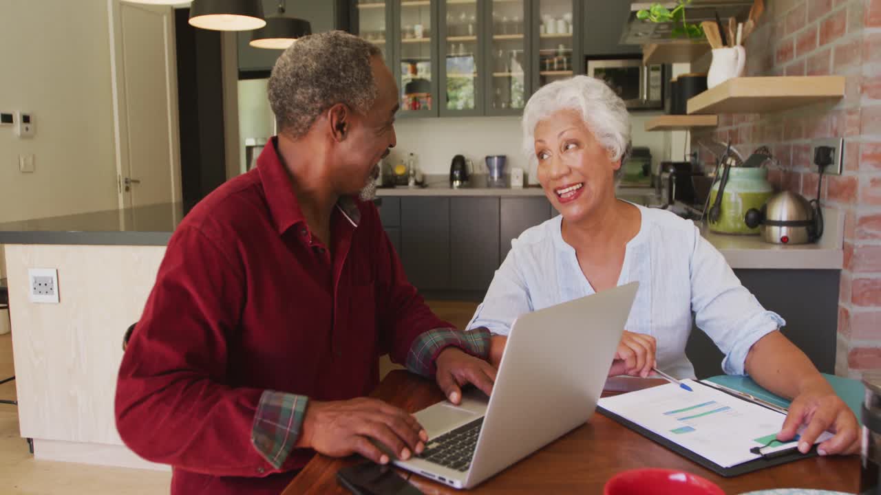Senior African American husband and mixed race wife happily working on a laptop at home