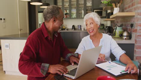 senior african american husband and mixed race wife happily working on a laptop at home