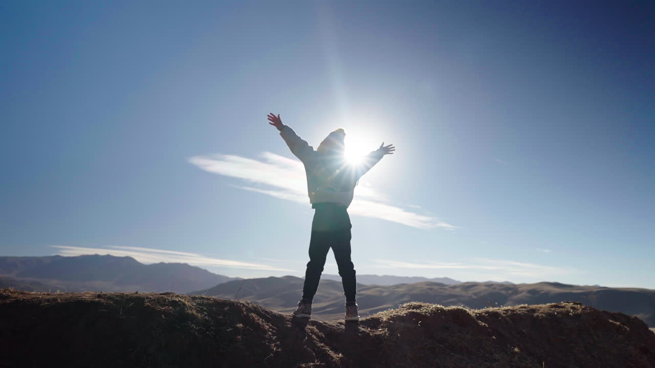 Silhouette of person raising arms in triumph against sunrise over mountain ridge
