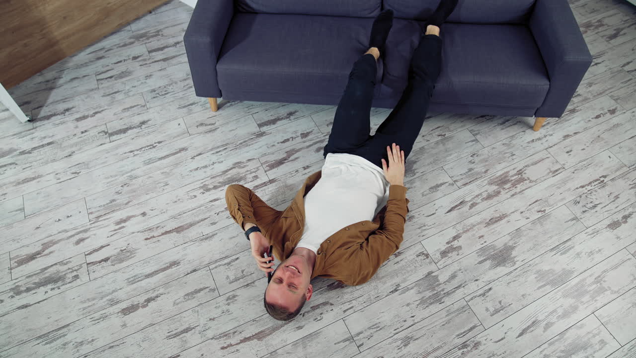 Man relaxing using mobile phone. Happy young man talking on mobile phone and lying on the floor