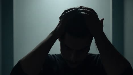 person holding head in hands, silhouette in dark room