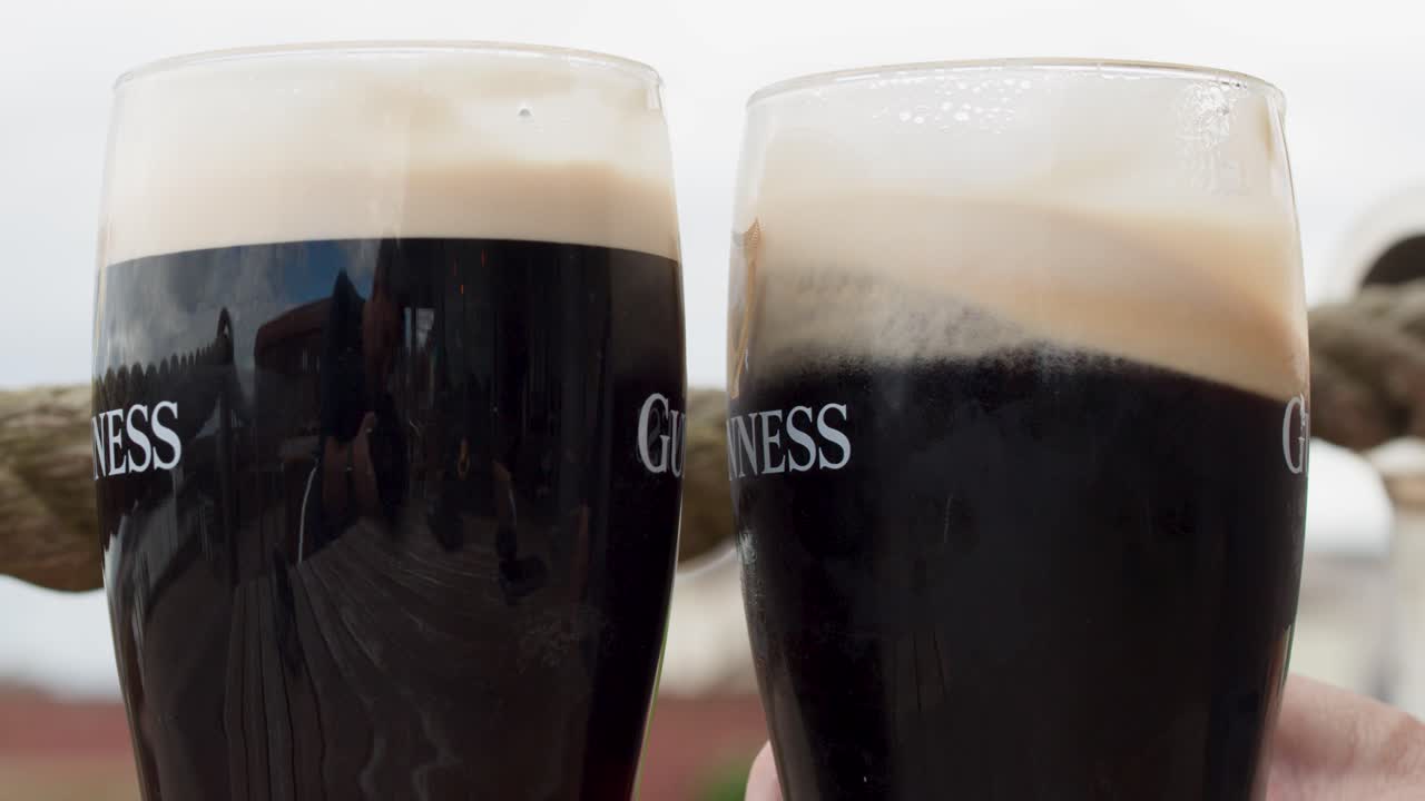 Two dark beers swirl and settle in natural daylight, close-up, outdoor setting, steady camera