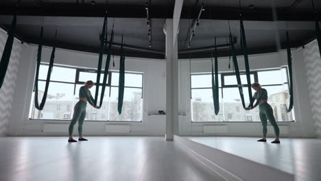 young smiling woman practice in aero stretching swing. aerial flying yoga exercises practice in green hammock in fitness club
