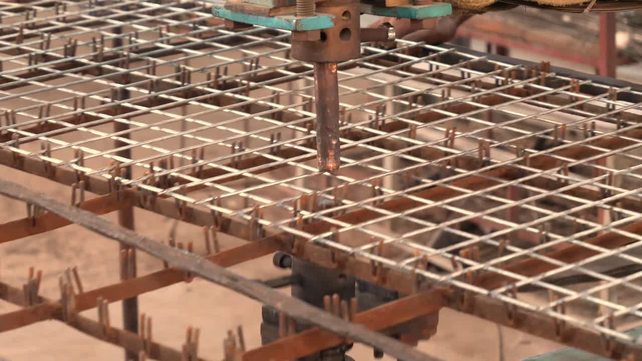 primer plano de la vista del brazo de la máquina de soldadura por puntos creando chispas en el bastidor de malla de alambre en la fábrica