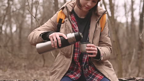 a young girl in a yellow woolen hat serves herself a hot beverage in the forest