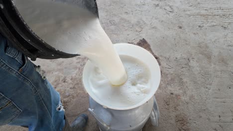fresh milk being poured into a container through a funnel, captured in a rustic setting