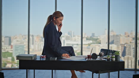 young businesswoman calling smartphone sitting on table barefoot at panoramic