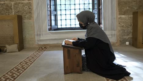 mujer sentada de rodillas y leyendo el corán