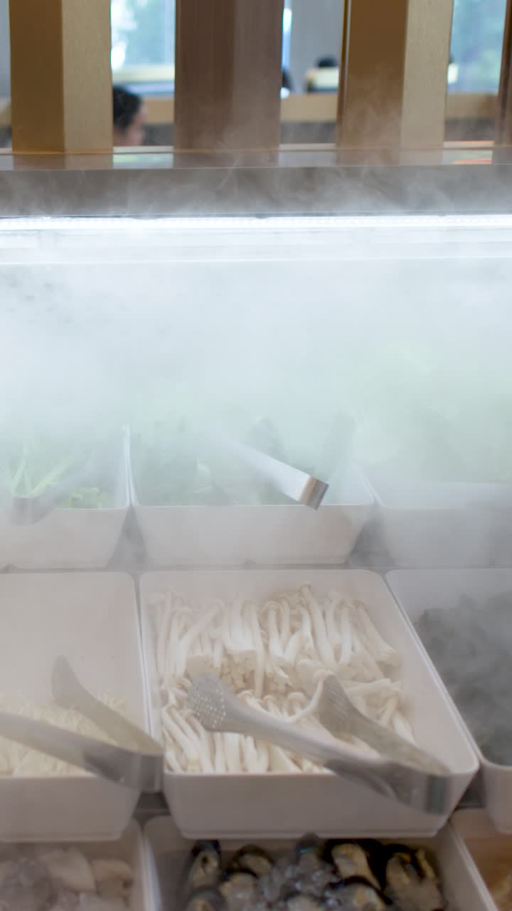 Una telecamera panoramica riprende un buffet refrigerato con verdure fresche sotto una nebbia d'acqua rinfrescante.