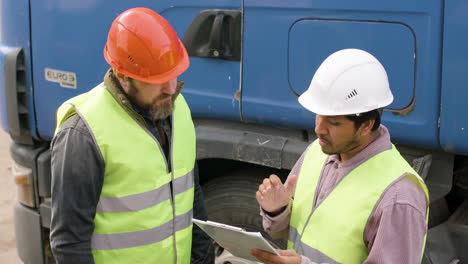 close up view of boss and worker wearing vests and safety helmets organizing a truck fleet in a logistics park while they consulting a document