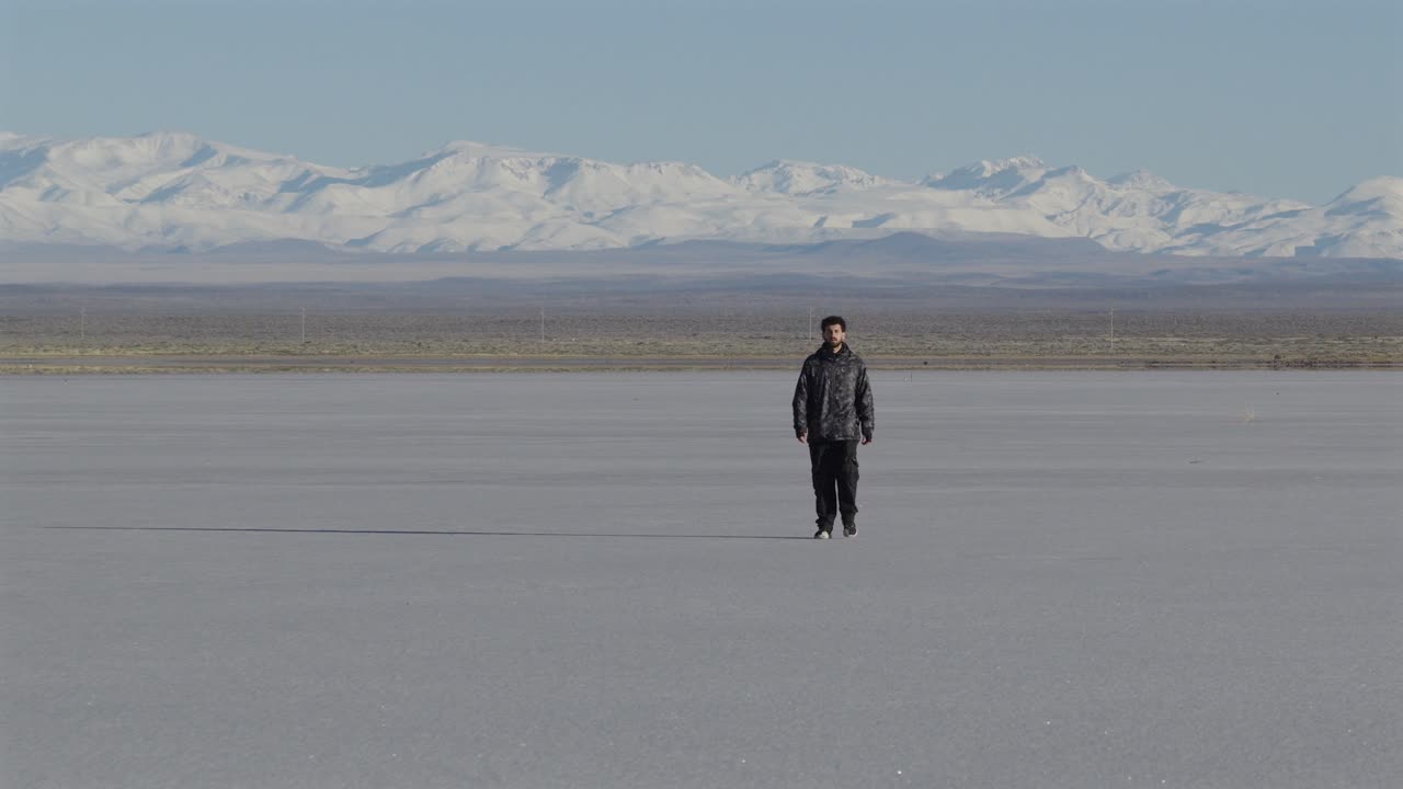 Aerial view of man walking alone on vast salt flat surrounded by snow-capped mountains, solitude, freedom, Mendoza, Argentina
