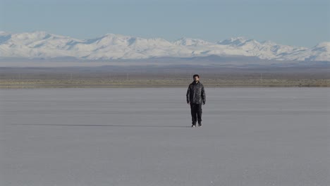 aerial view of man walking alone on vast salt flat surrounded by snow-capped mountains, solitude, freedom, mendoza, argentina