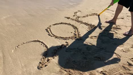 a man writing "2018" with the stick end of the shovel on a sandy beach in oahu, hawaii