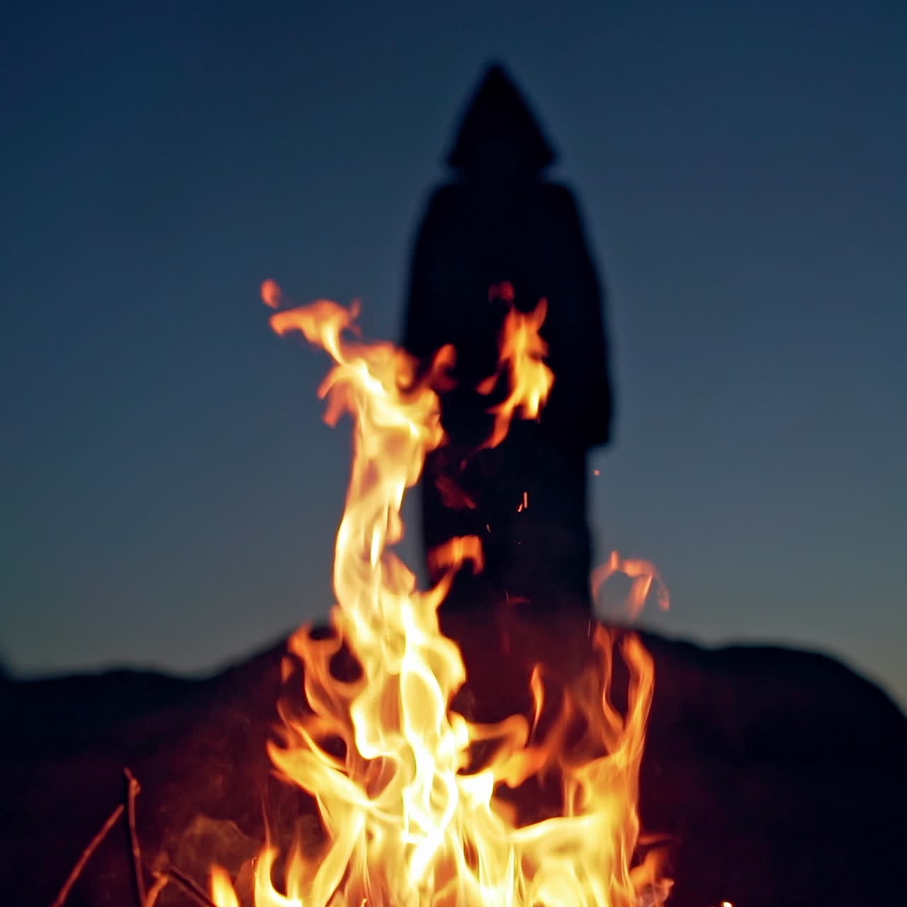 Evil witch hooded creature walking around the fire. Halloween costume