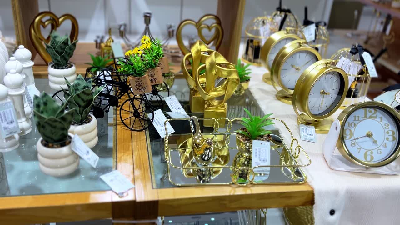 Stylish tabletop display of home decor items, including gold clocks, indoor plants, ceramic pots, and decorative ornaments. Perfect for lifestyle, design, and retail themes in 4K clarity.