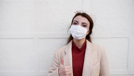 beautiful girl wearing protective medical mask and fashionable clothes does thumbs up gesture