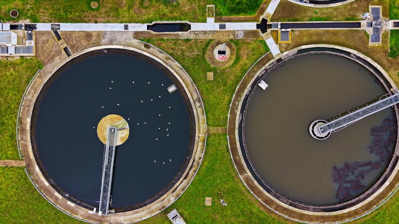 Water treatment facility with large circular tanks and machinery under bright sunlight during midday