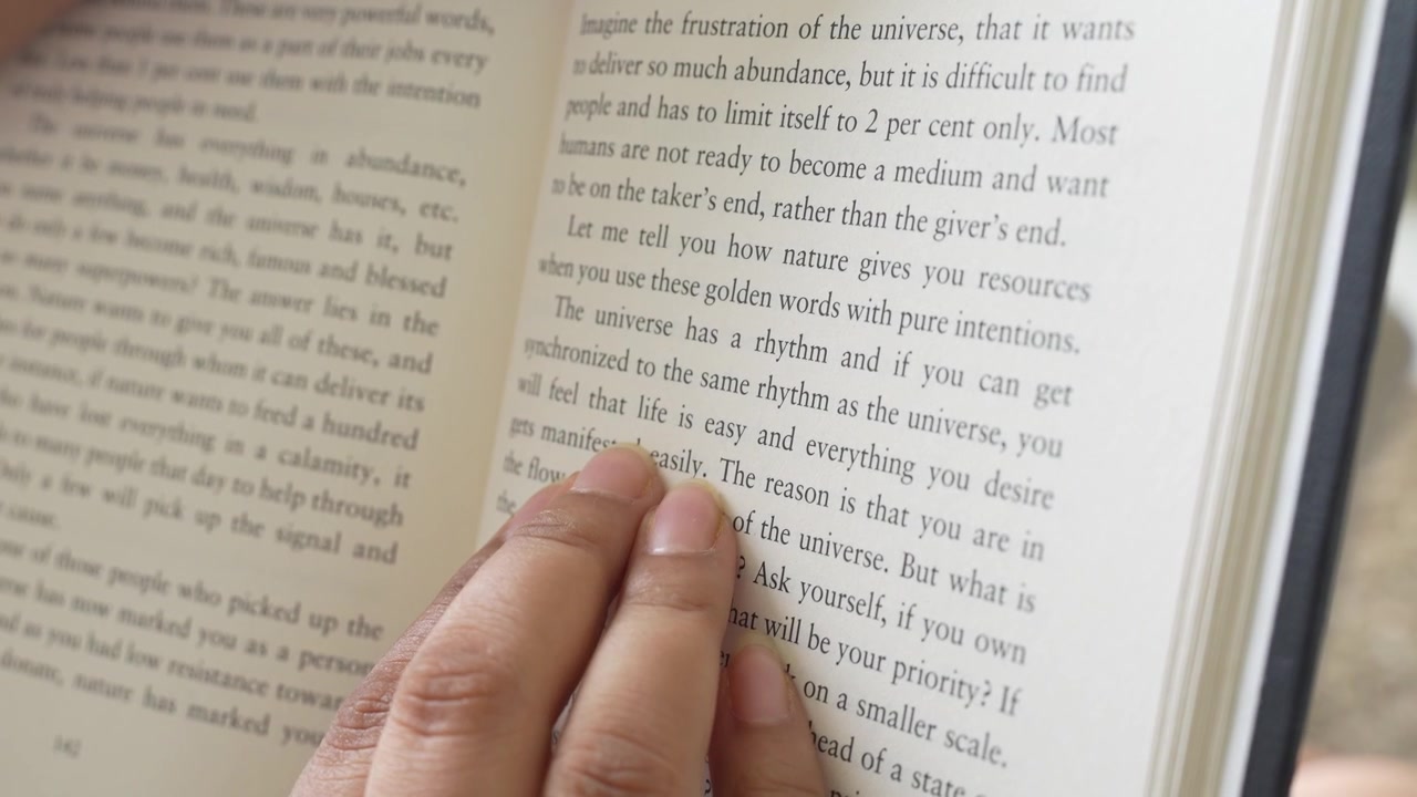 Close-up of a woman's hand gently pressing and smoothing an open book page while reading, with clearly visible printed text and soft natural window light illuminating.