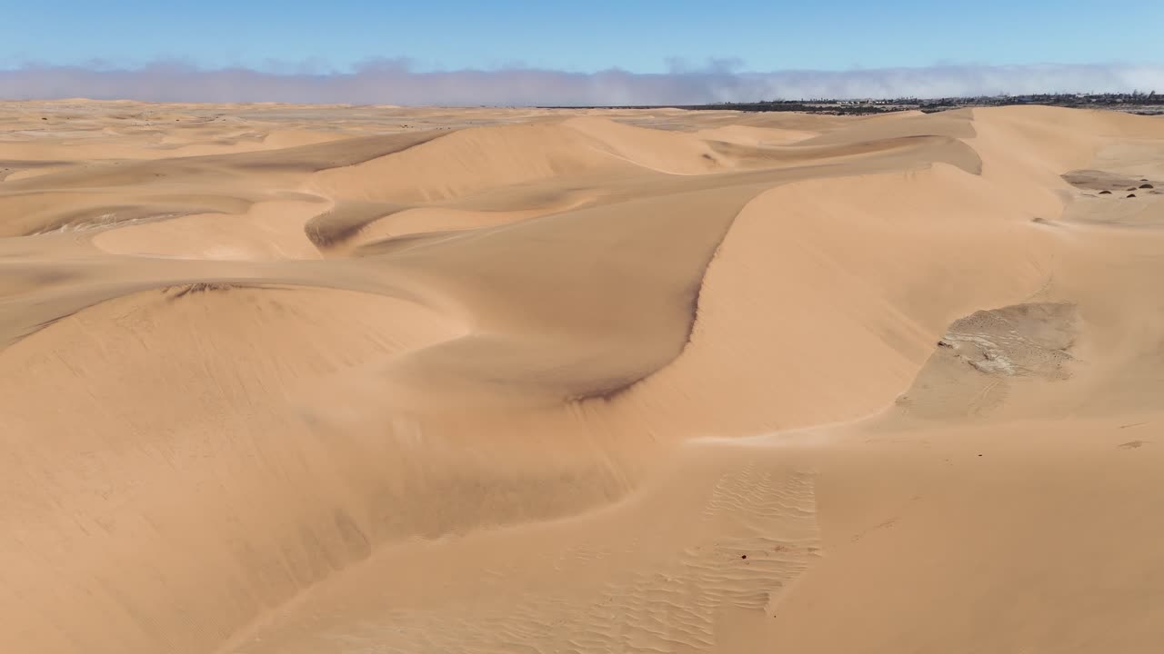 Aerial cinematic view of Swakopmund’s sand dunes merging with the ocean, capturing Namibia’s stunning desert-to-sea landscape