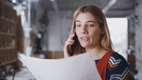 Female-Business-Owner-In-Workshop-For-Building-Bicycles-Making-Call-On-Mobile-Phone