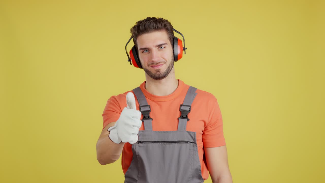 Man in work overalls and earmuffs gives thumbs up