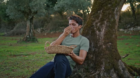 hombre positivo olor a olivo paisaje de árbol de cerca. feliz granjero teniendo descanso