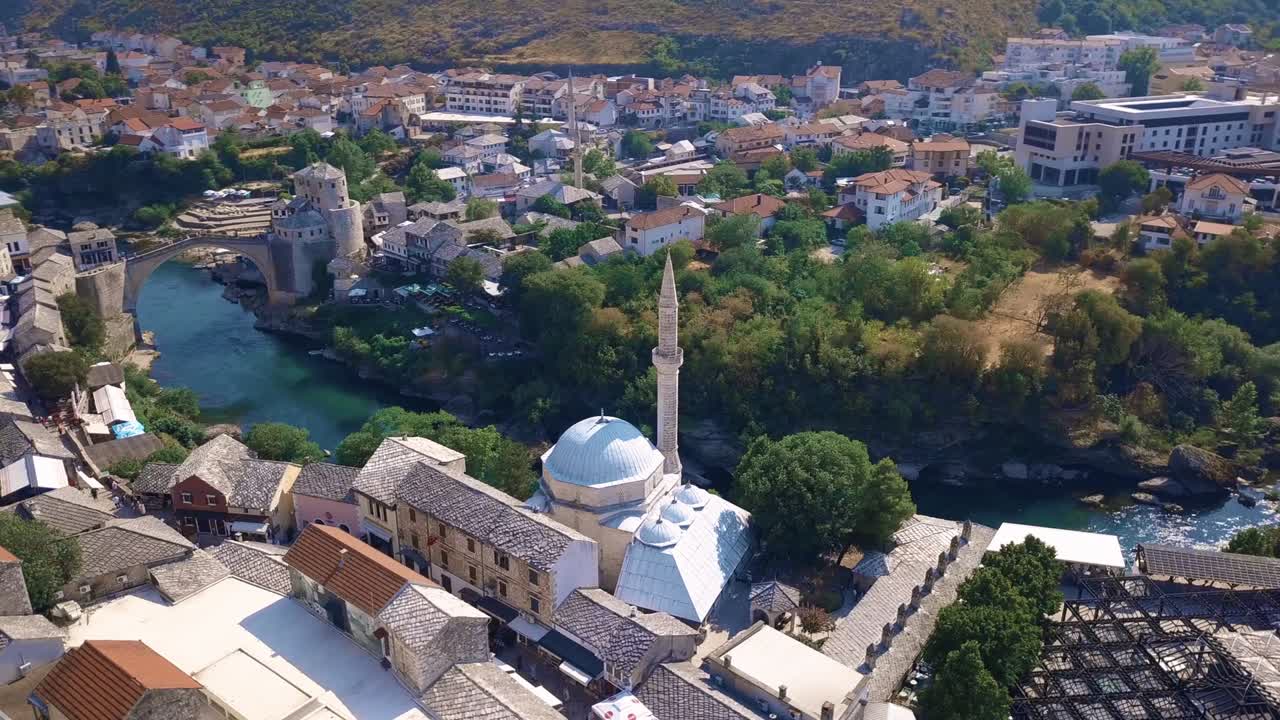Circling drone shot of a mosque in Mostar with famous bridge in the background