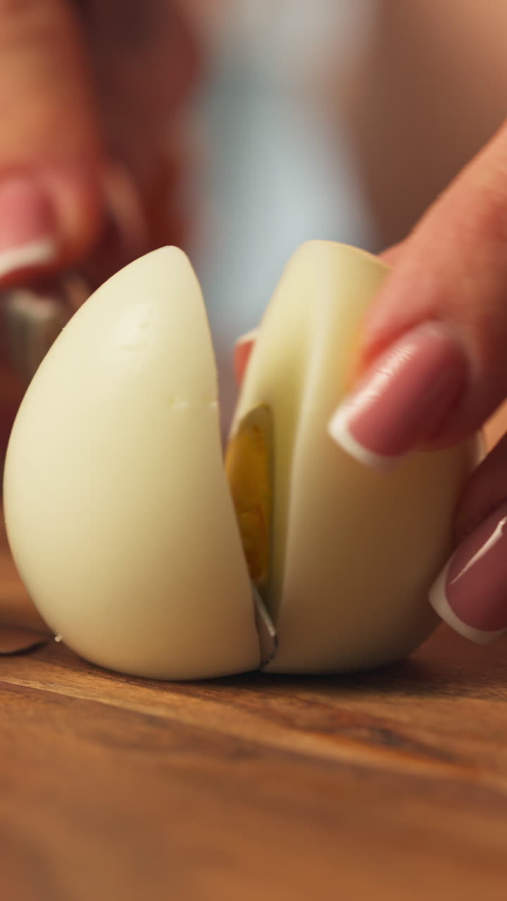 Woman Slicing Hard-boiled Egg In Half With A Knife. - closeup, vertical shot