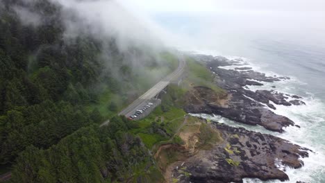 4k 30fps aerial footage oregon coast - epic tracking shot of us route 101 and car traffic- flying amongst clouds, waves crashing against mossy stone rocky pacific ocean shore - dji drone video