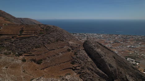 Aerial-view-around-bare-mountains-on-the-Santorini-island,-in-sunny-Greece---rotating,-pull-back,-drone-shot