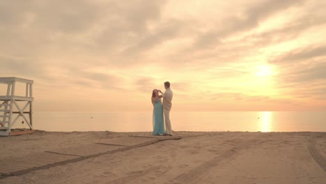 pregnant couple on sea beach. man straighten hairs of his pregnant woman