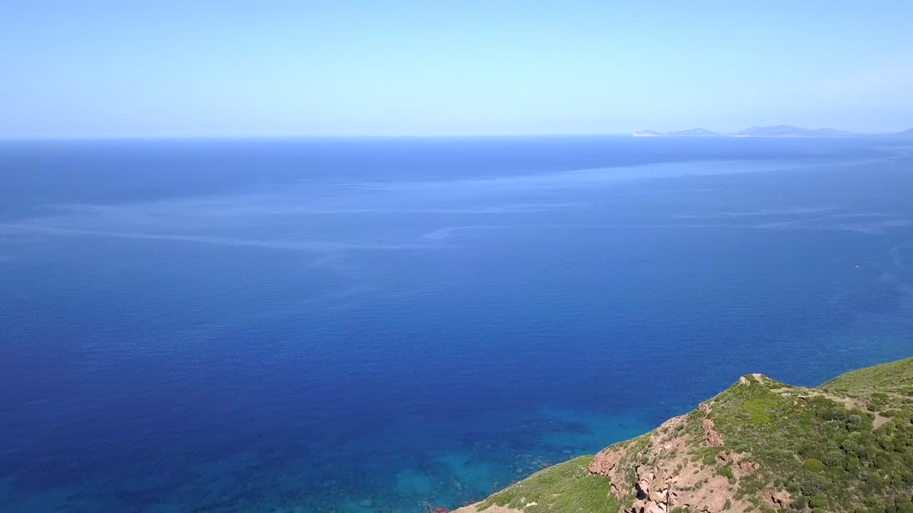 Drone Aerial shot, flying backwards over a stunning blue Mediterranean Sea and discovering the green cliffs along the coast on the island of Sardinia in Italy