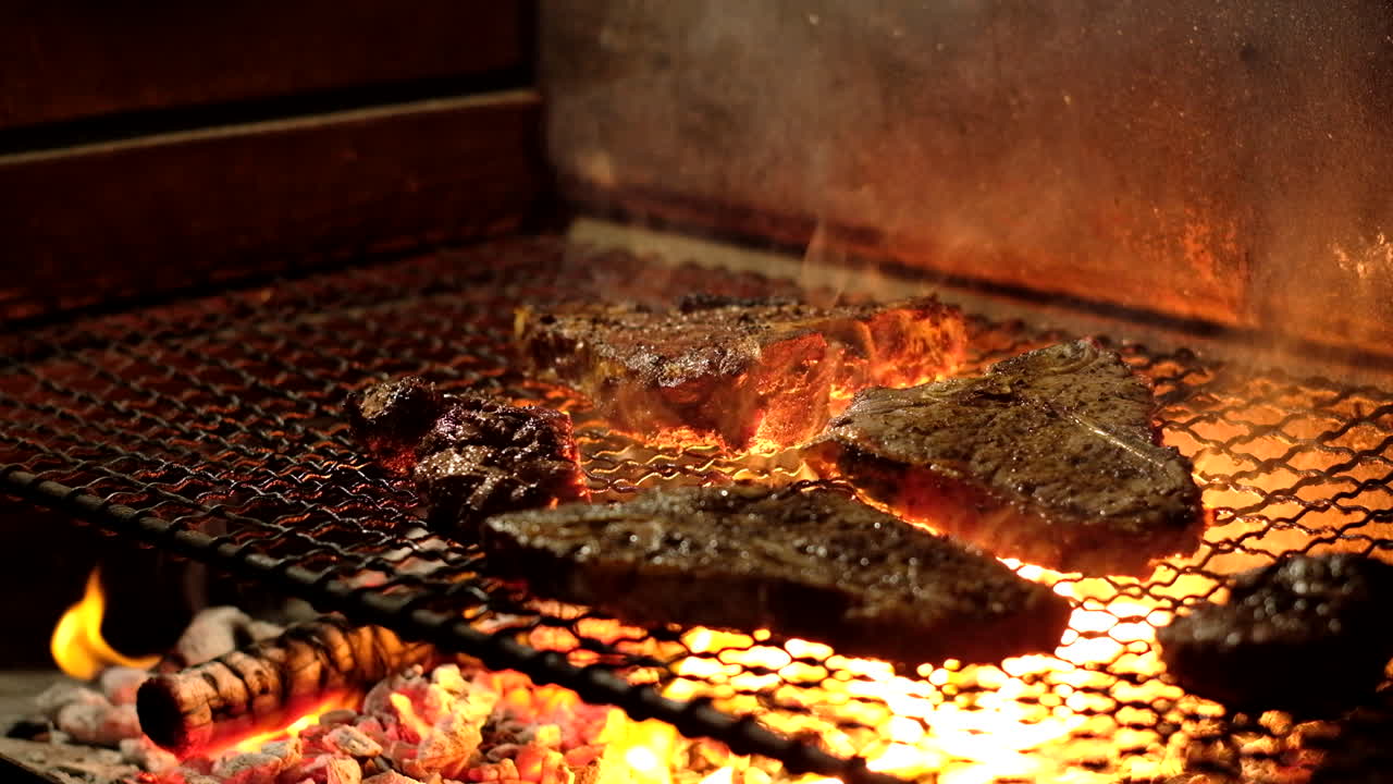 Tongs used to flip and grill juicy beef steaks on hot coals with licking flames