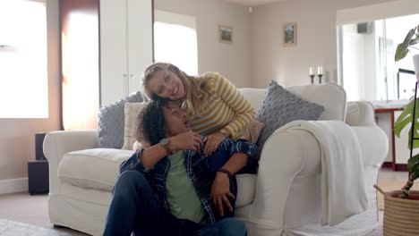 retrato de una feliz pareja diversa abrazándose y sentada en el sofá en casa, en cámara lenta