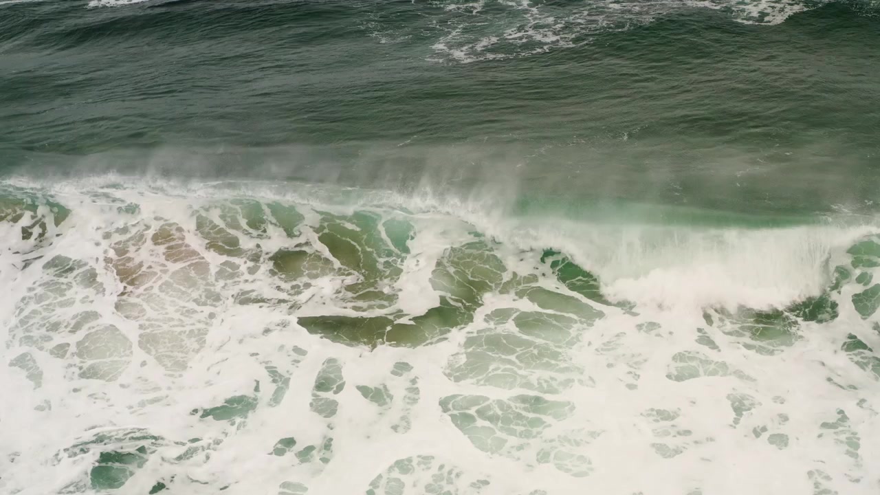 Top-down drone view of turquoise wave breaking with white foam on wild Scottish beach.