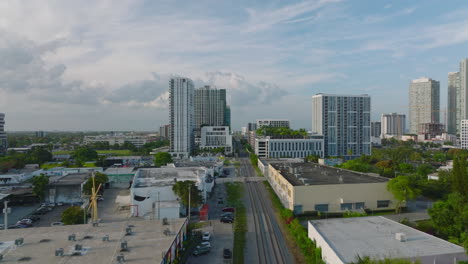 Elevated-view-of-green-vegetation-and-buildings-in-city.-Vehicles-driving-on-road-and-crossing-railway-tracks.-Miami,-USA