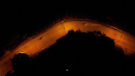 aerial drone shot of two motorbikes driving down an empty road with yellow streetlights at night in a rural area on koh pangan island, thailand