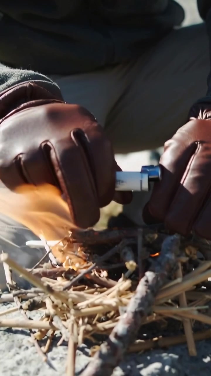 Vertical video: Striking lighter, senior man with gloves kneeling on rock, igniting tinder for fire