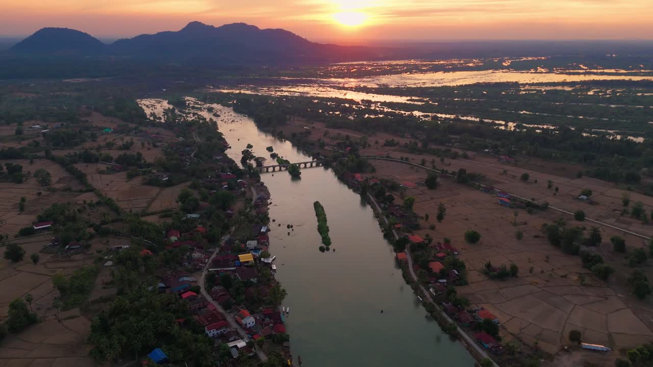 Scenic Aerial landscape fly Rural River Village in Laos, 4000 Islands, sunset reflected on water around traditional village